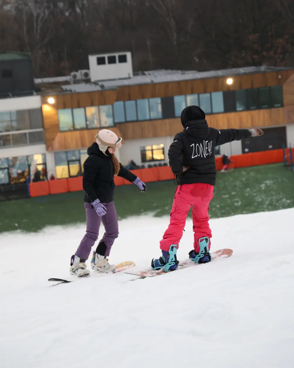 Instruktorka Zone4 w kurtce z napisem ZONE4 uczy kursantkę jazdy na snowboardzie na Górce Szczęśliwickiej