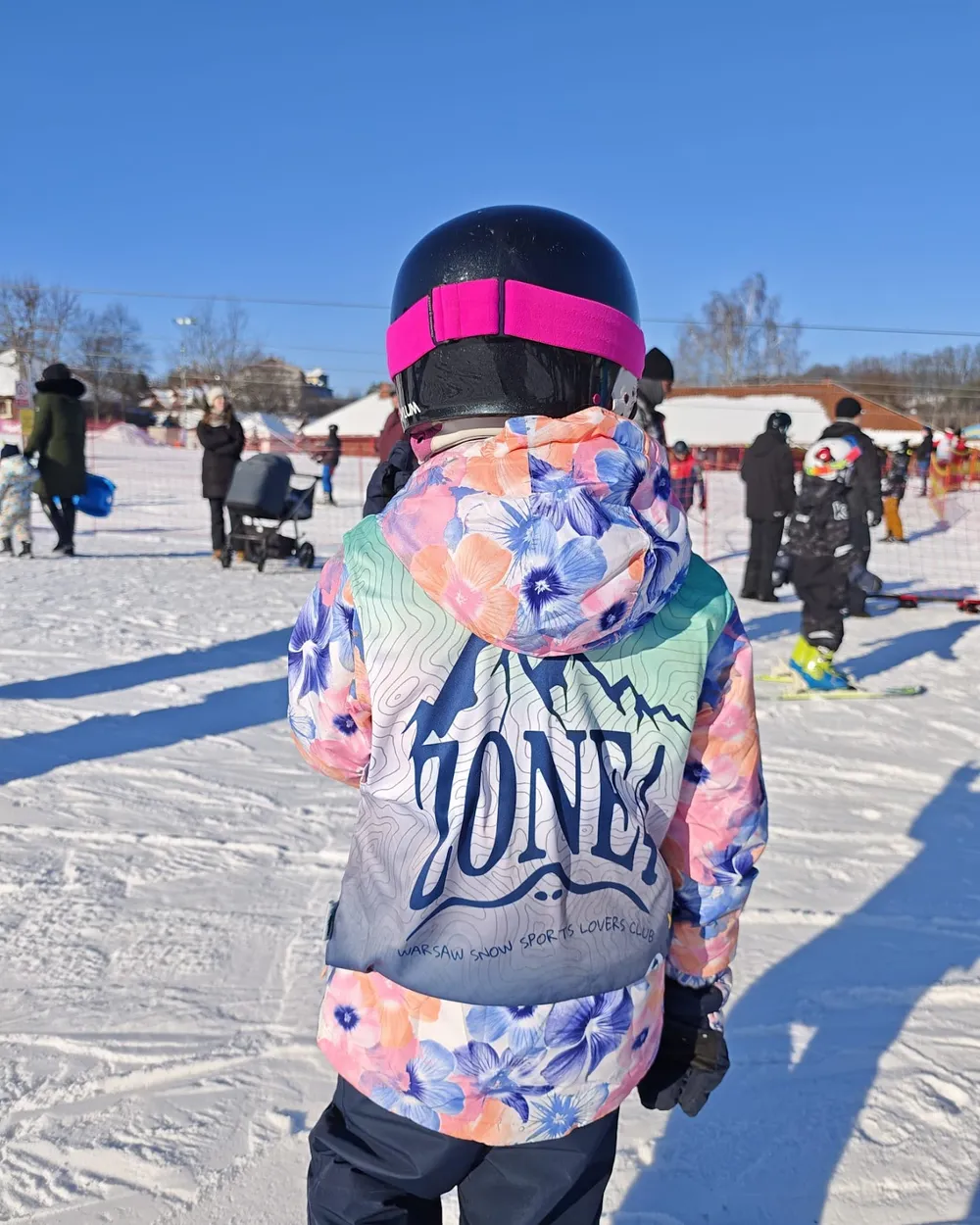 A child in a Zone4 jacket on the slope during a ski trip, seen from behind